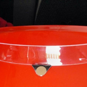 Mein neuestes Windschild ist aus einem kratzfesten Helmvisier mit der Laubsäge ausgesägt. In der Mitte ist an einem 2mm dicken Gummi, der mit Sekundenkleber am W-Schild angeklebt ist, ein Magnet. Das W-Schild ist mit Spannung zwischen den beiden Rückspieg