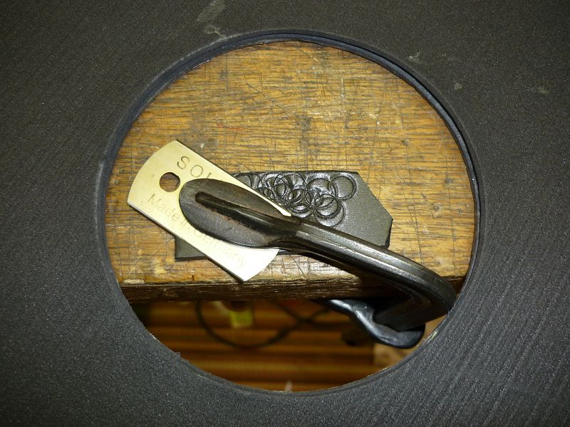 Radkappe-7. 
Um die Kontur an die Bremstrommel anzupassen, ist hier eine Herdplatten-Schabeklinge über eine Beilage am Tisch festgespannt. Durch Drehen der Radkappe kann man einen parallelen Einschnitt in der Bohrung erzeugen. Das zu entfernende Stück wi